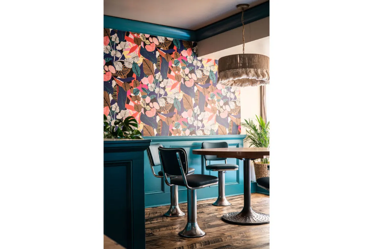 A contemporary dining space with a floral patterned wall, modern chairs, a stylish pendant light, and a wooden table set for casual gatherings. The ambiance is cheerful and relaxed, ideal for in-room dining or leisurely meals.