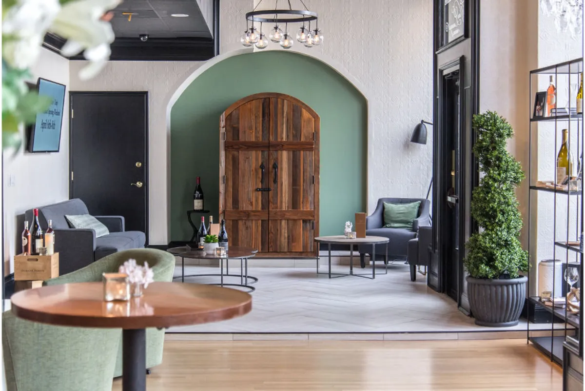 An inviting in-room seating area centered around a modern wooden door and a green accent wall. The seating arrangement is intimate, complemented by shelves with bottles, hinting at an honor bar. Warm lighting and a stylish setting set the mood for relaxation or cozy gatherings, evoking the ideal nook for morning coffee or evening card games.