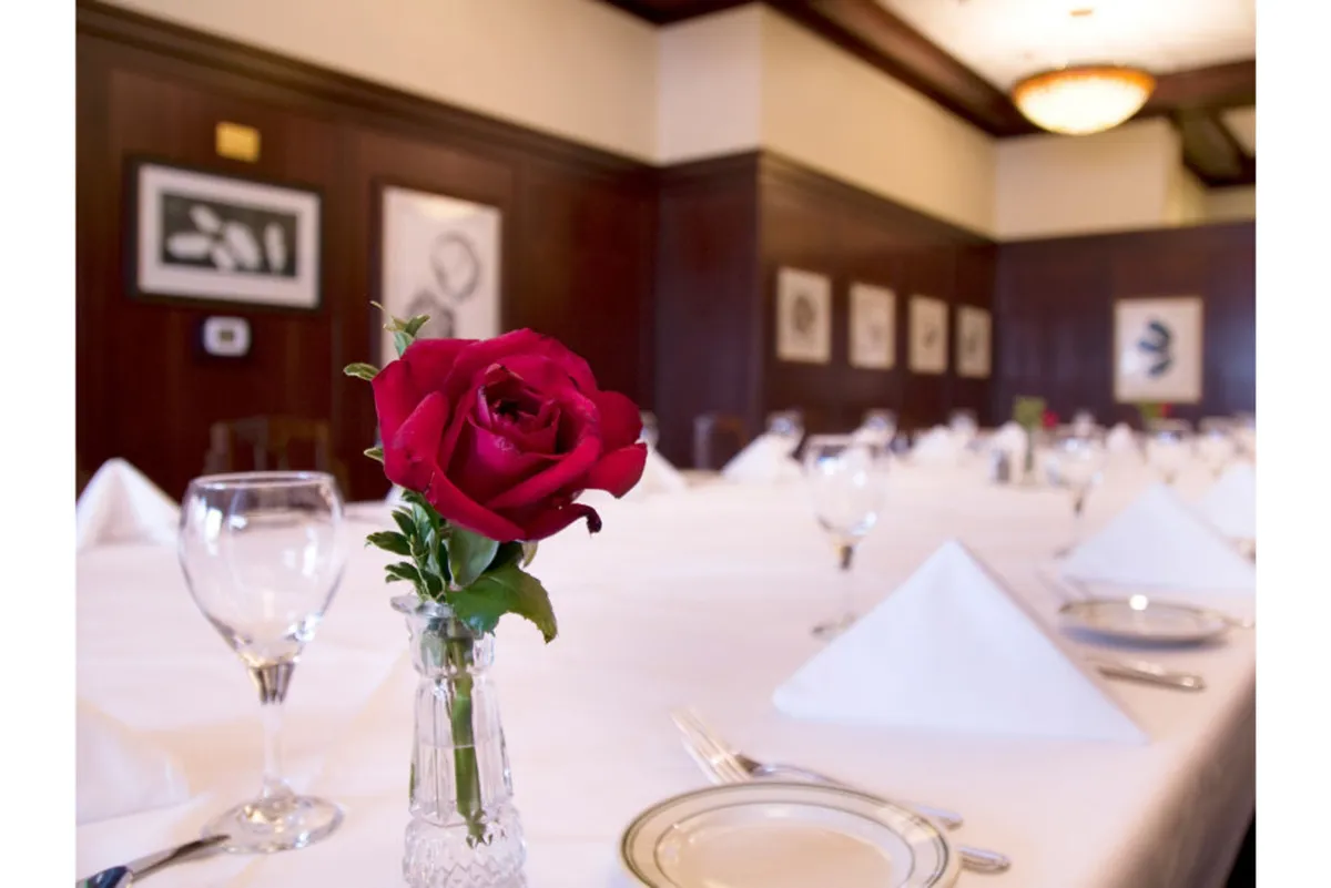 Inside, a sophisticated dining table setup is highlighted by a vibrant red rose in a vase and framed wall art, capturing an ambiance suitable for both business meetings and moments of relaxation. The inviting mood is perfect for guests seeking productivity as well as comfort.