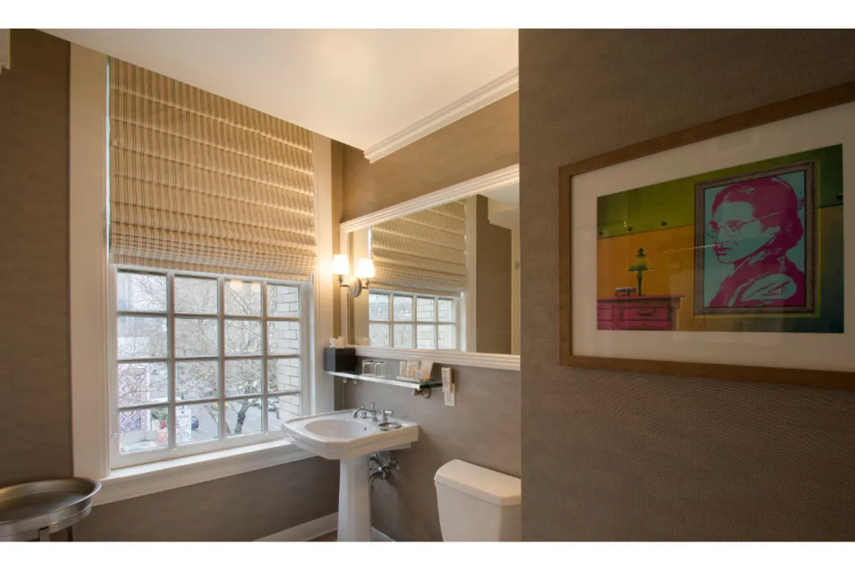 A calm and stylish hotel bedroom featuring a tastefully designed sink and mirror area, complemented by curated artwork on the walls. Soft natural light filters through a window, highlighting the elegant and functional details. The scene exudes comfort and sophistication, reflecting a personal sanctuary ideal for relaxing or preparing for the day.