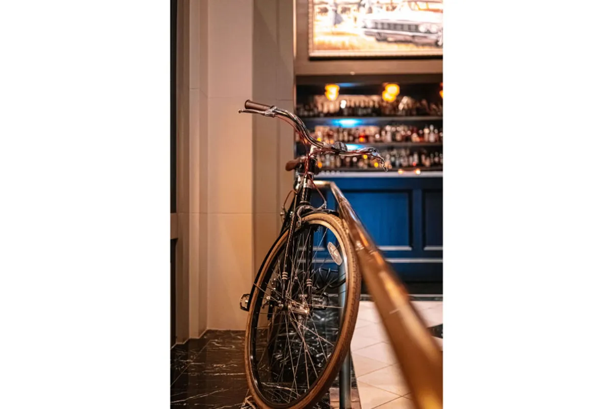 A casually stylish bar area highlighted by industrial lighting fixtures and a vintage bicycle mounted as decor. The space features a sleek bar, comfortable seating, and design elements that blend modern Portland vibe with playful touches, offering an inviting spot to relax after a day outdoors.