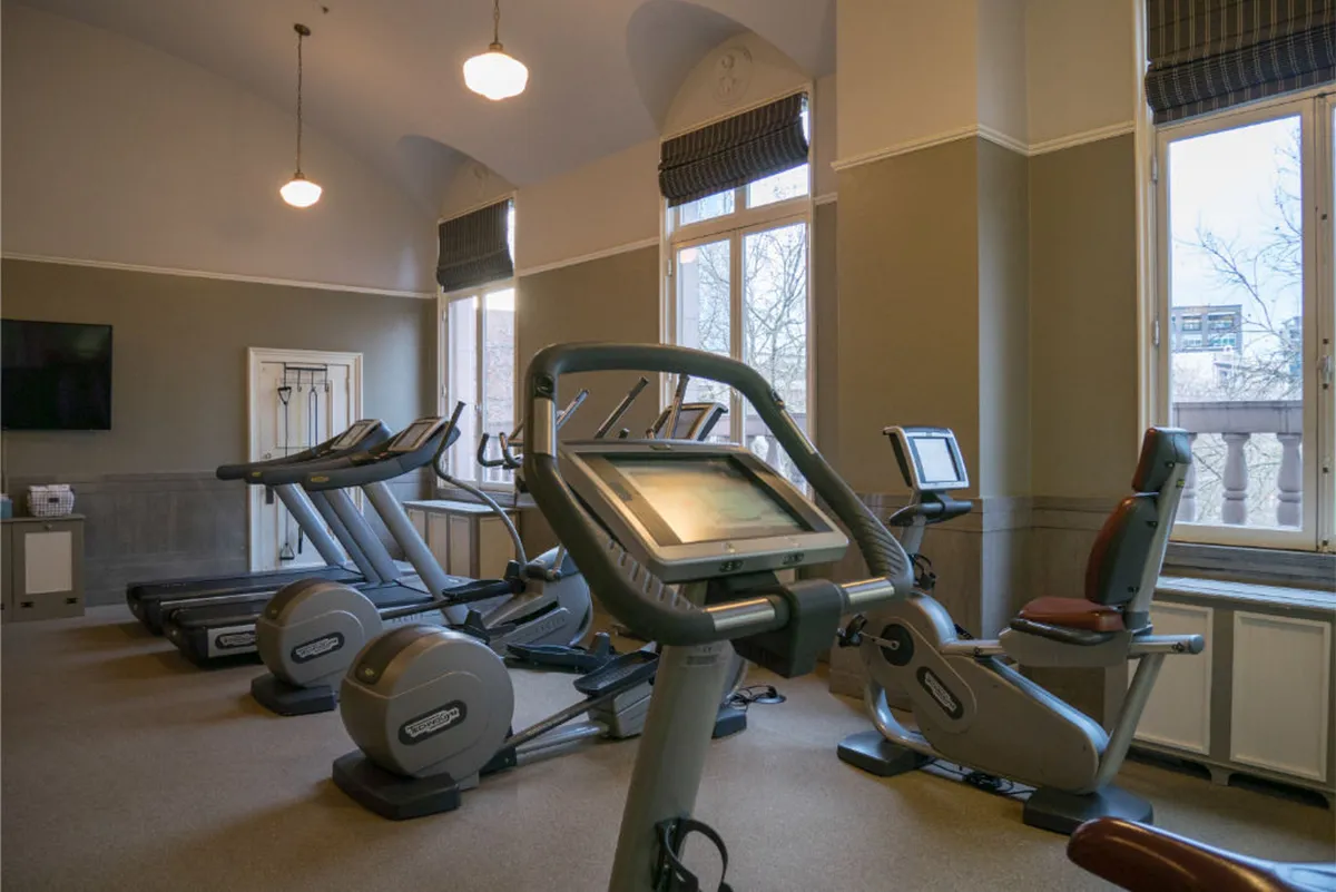 A bright, motivational fitness center with large windows allowing natural light to fill the space, featuring modern exercise equipment and a television screen. The setup is ideal for both solo workouts and group activities, capturing an energetic and uplifting mood.