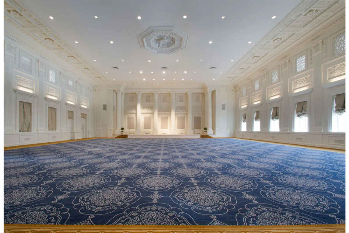 A grand interior with an ornate ceiling design, intricate carpet patterns, and large windows draped with soft fabrics. The space is illuminated with warm light, creating a regal and inviting mood suitable for romantic gatherings and special occasions.